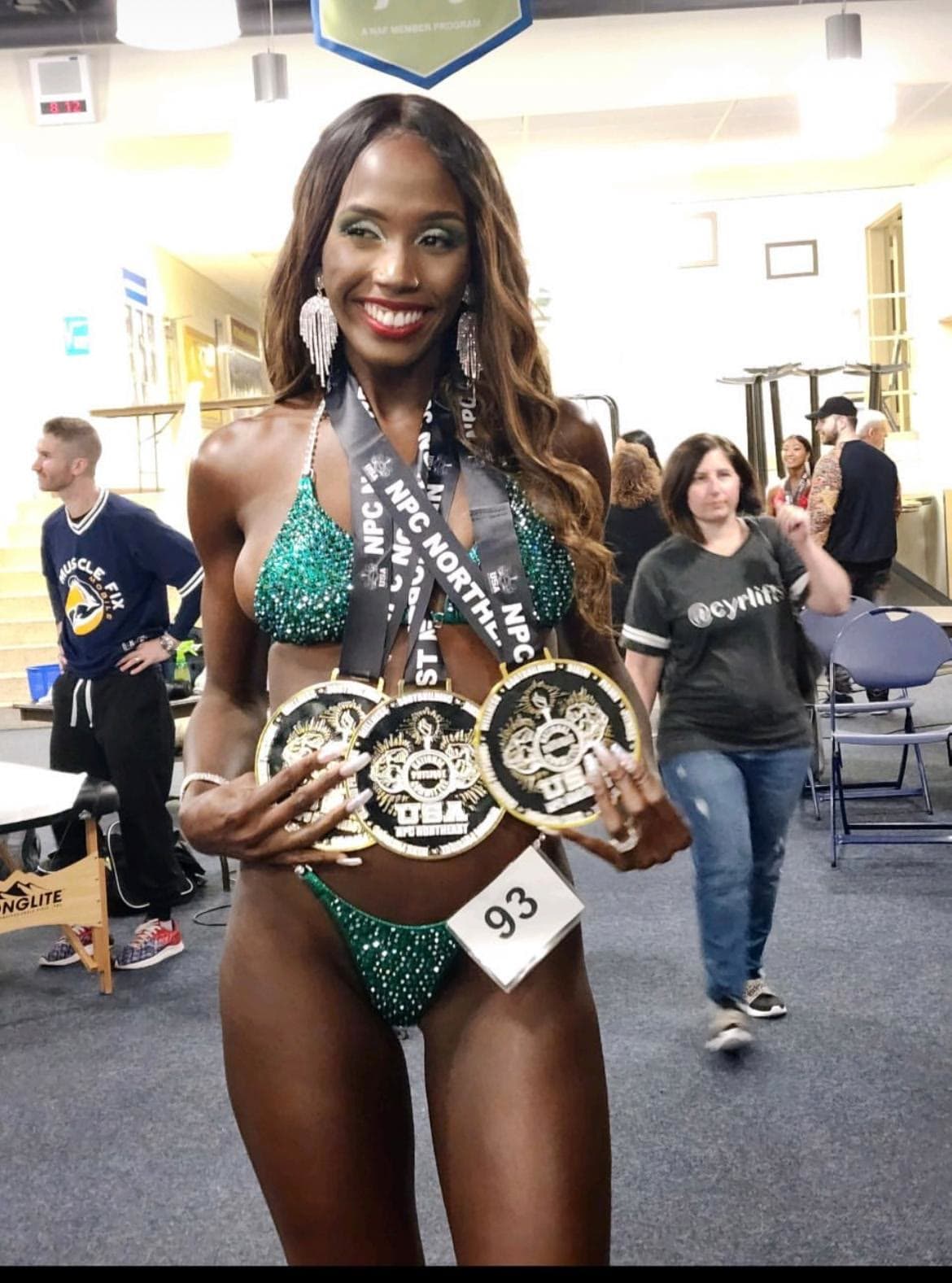 A bikini competitor holding up her medals backstage
