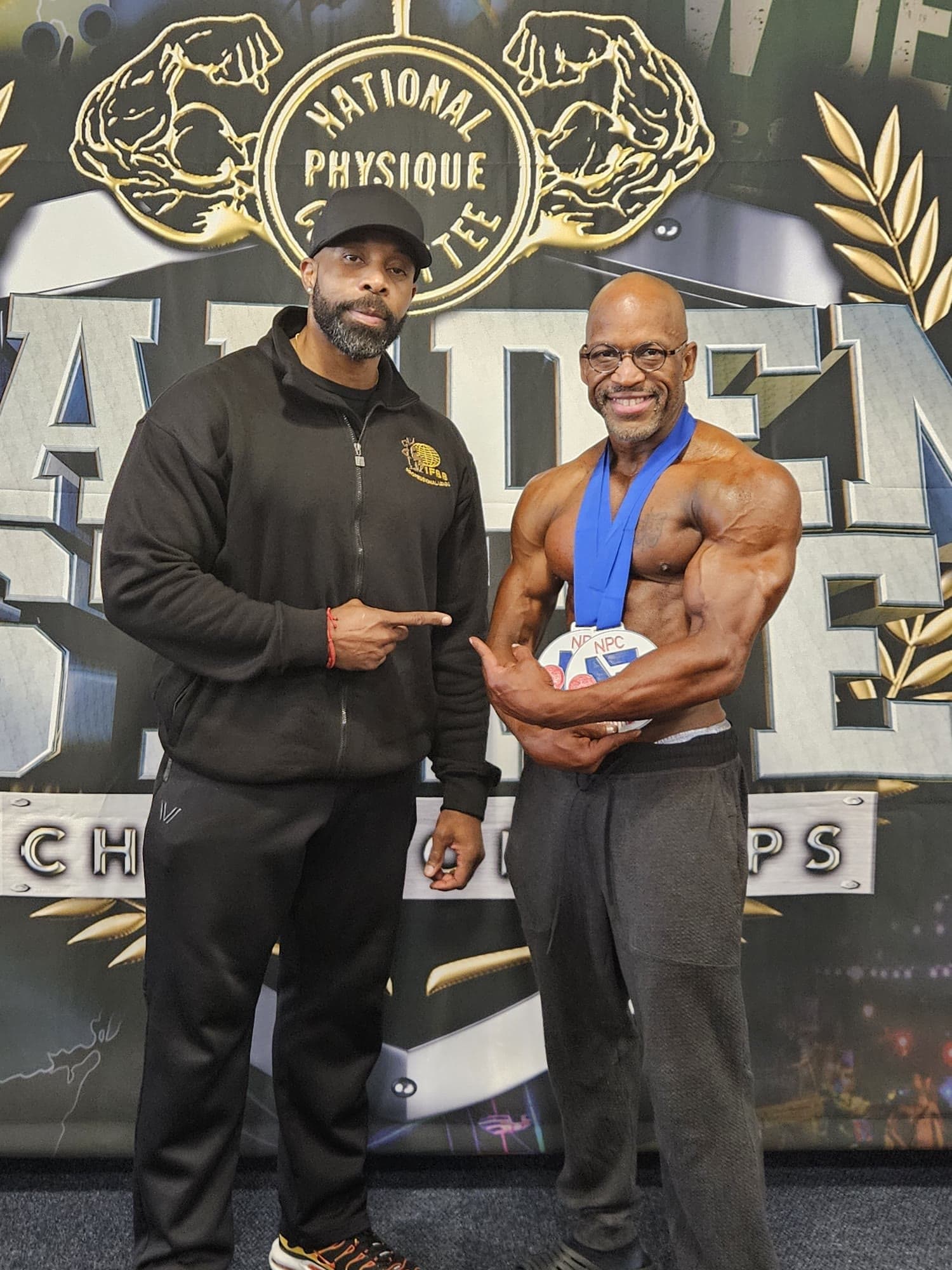 Daine Chang pointing at a competitor holding his medal in front of a show backdrop