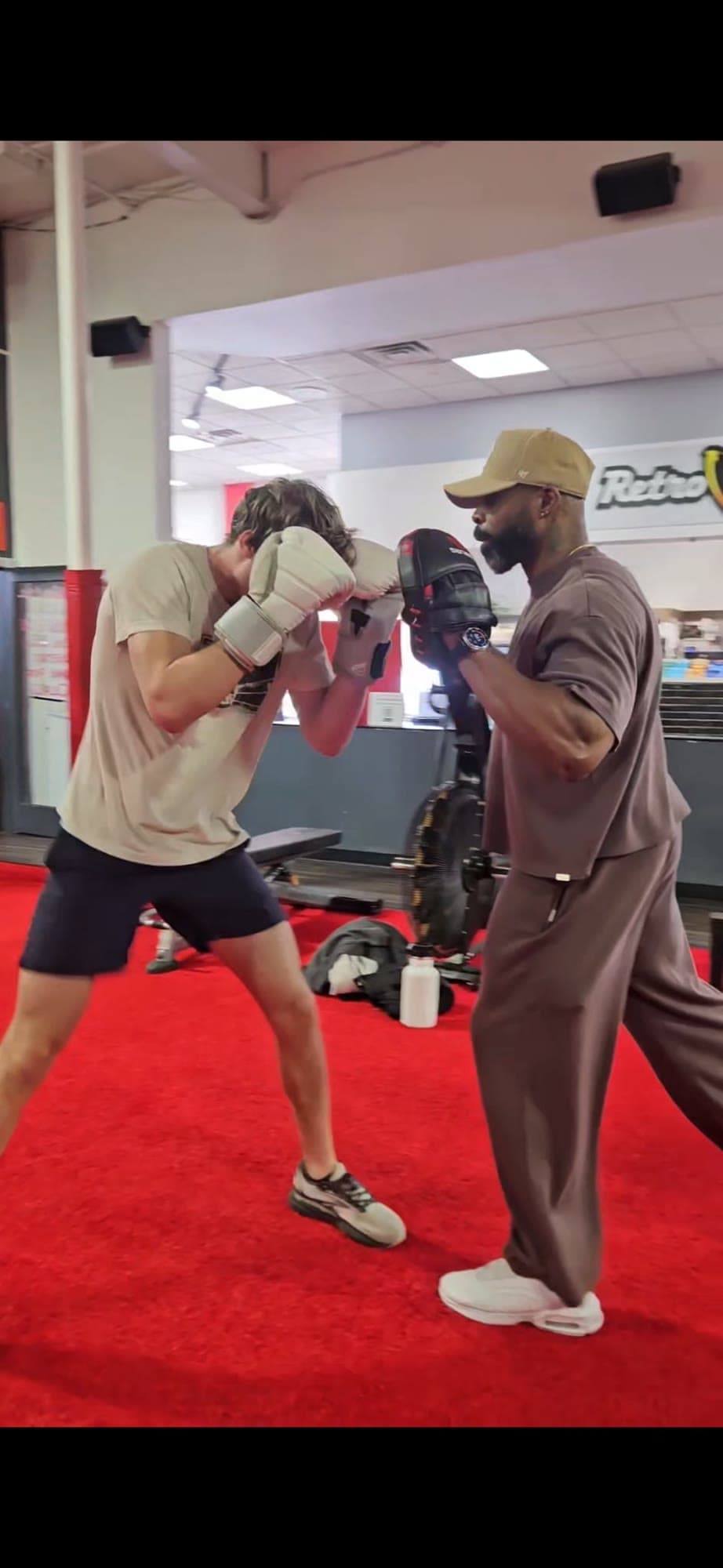 Daine Chang holding pads for a client on a red gym floor