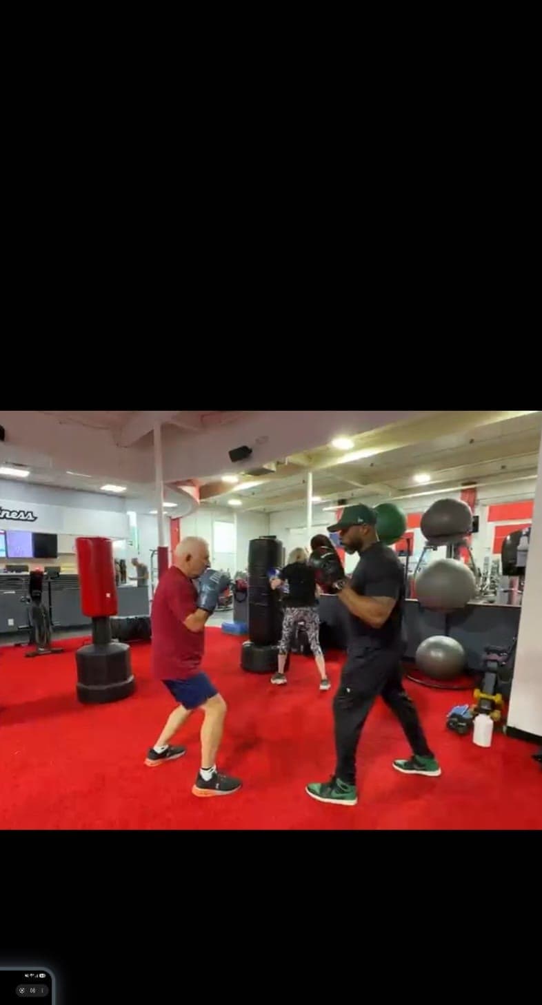 A client working the pads with Daine Chang on a red gym floor