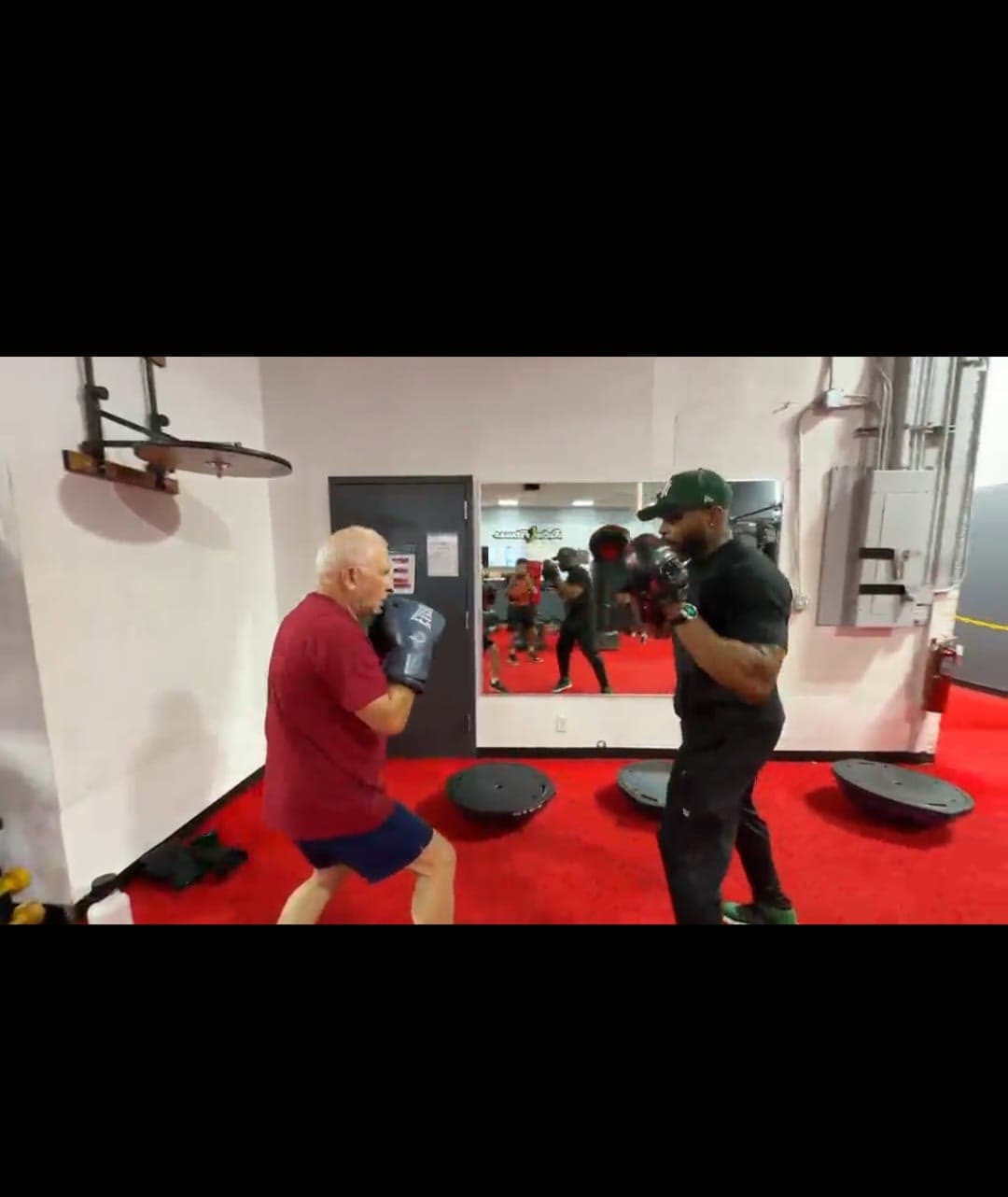 Daine Chang holding pads for an older client on a red gym floor